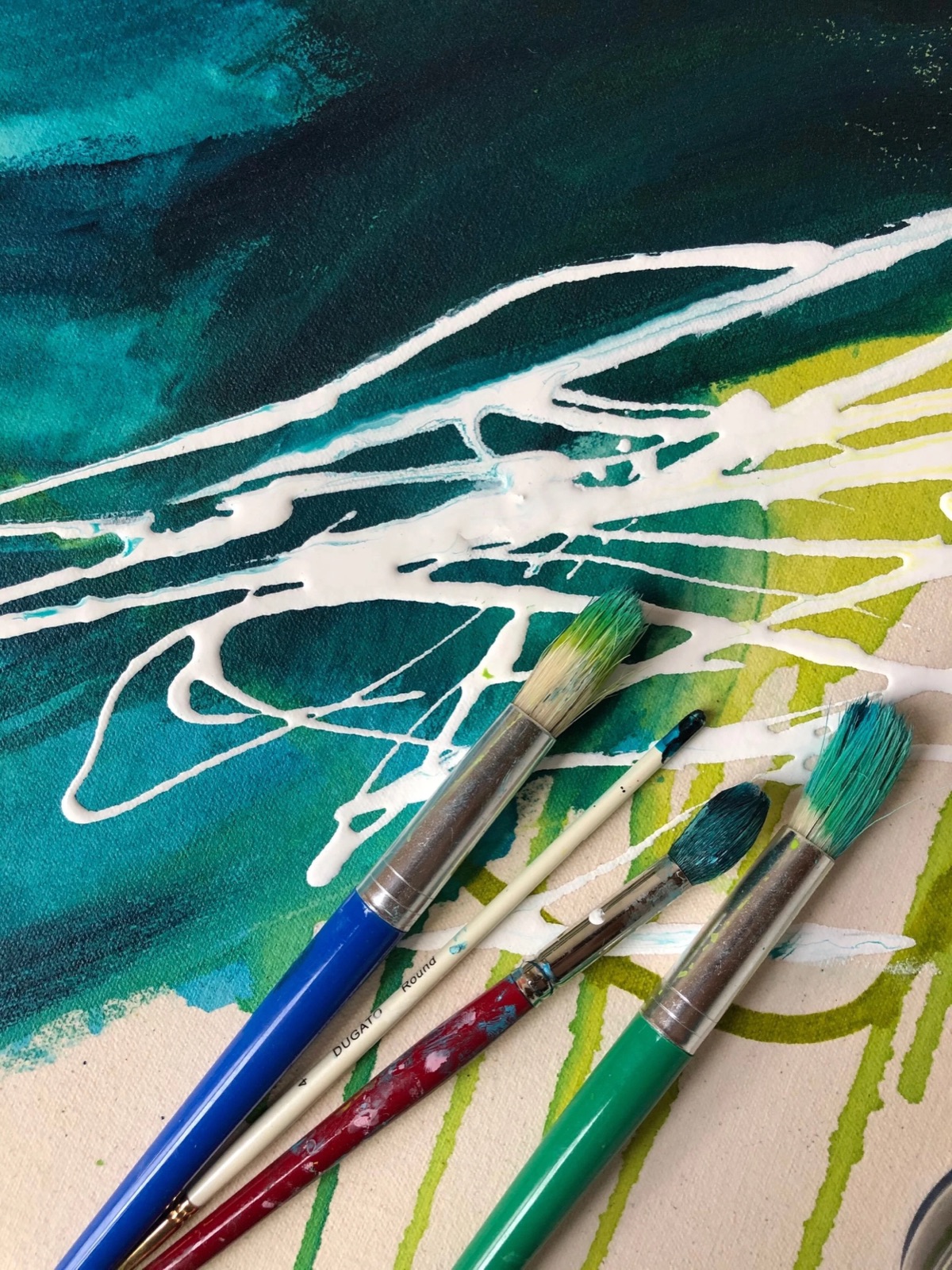 Brushes resting on a wet teal and green painting in Brooke Duncan's studio